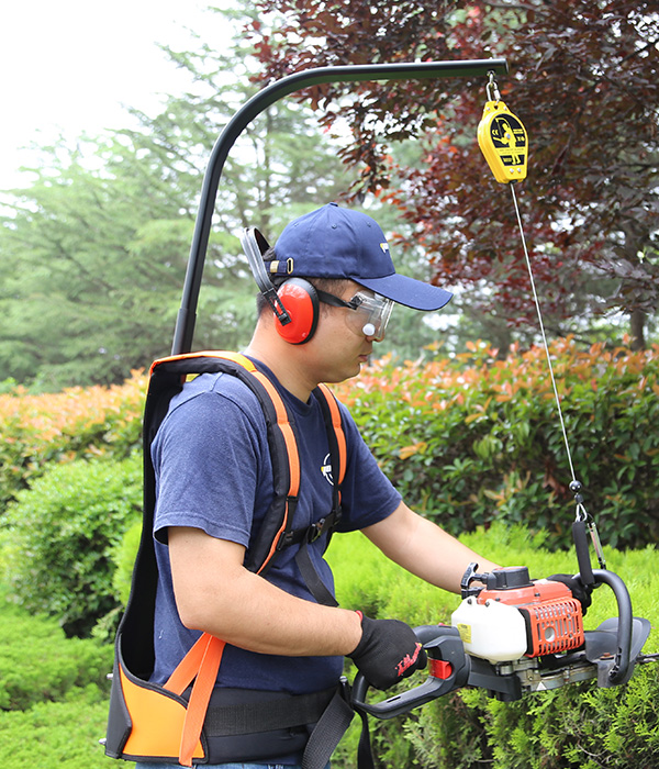 a man wearing safety gear and goggles holding a trimmer with help of harness